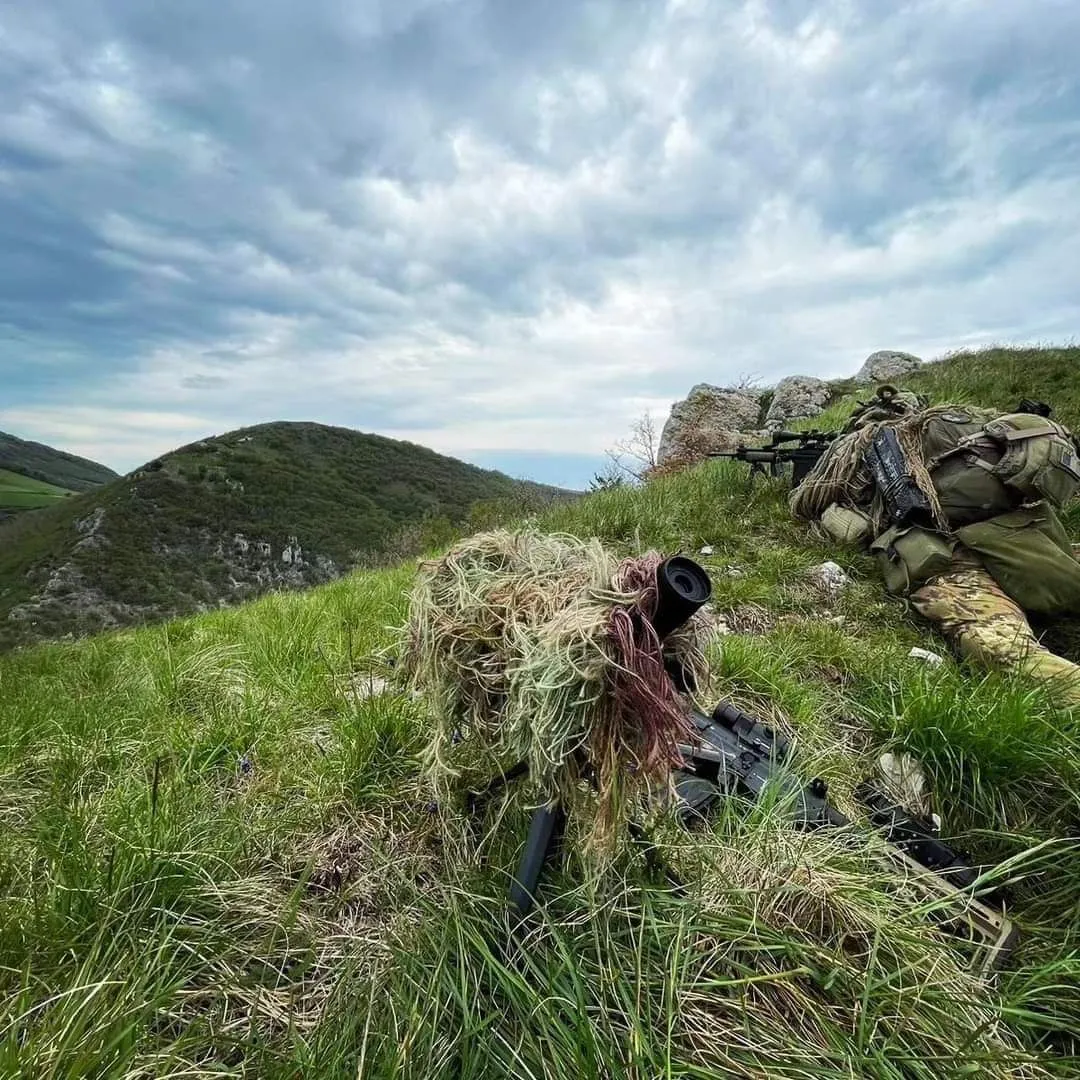 A pair of X-Tag snipers in ghillie suits, lying in wait on a grassy ridge